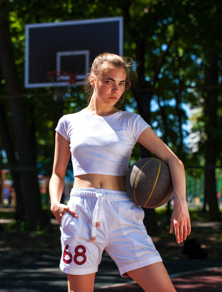 Молодая красивая девушка с баскетбольным мячом позирует на детской площадке
 - Фото, изображение