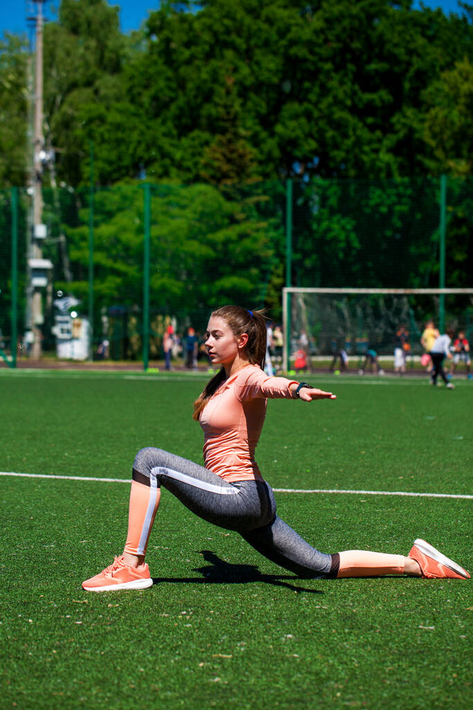 Ελκυστικό σπορ κορίτσι στα αθλητικά κάνει ασκήσεις τεντώματος στο στάδιο. Γυμναστική γυναίκα κάνει προθέρμανση προπόνηση. - Φωτογραφία, εικόνα