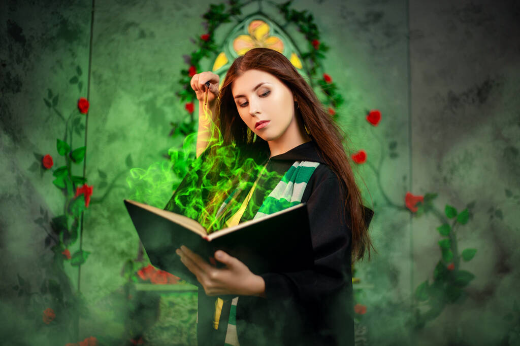 Siyah mantolu genç bir kadın boynunda çizgili bir eşarpla bir kitaptan bir büyü yapıyor ve sihirli bir değnekle büyü yapıyor.. - Fotoğraf, Görsel