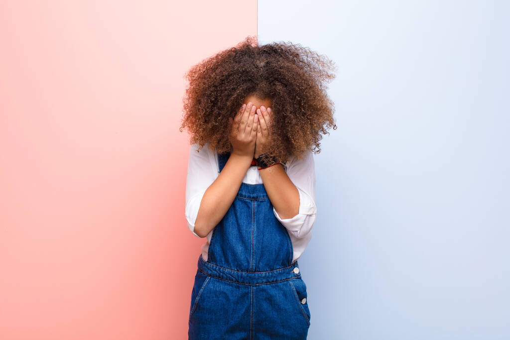 Afrykanka amerykańska dziewczynka smutna, sfrustrowana, nerwowa i przygnębiona, zakrywająca twarz obiema rękami, płacząca o płaską ścianę - Zdjęcie, obraz