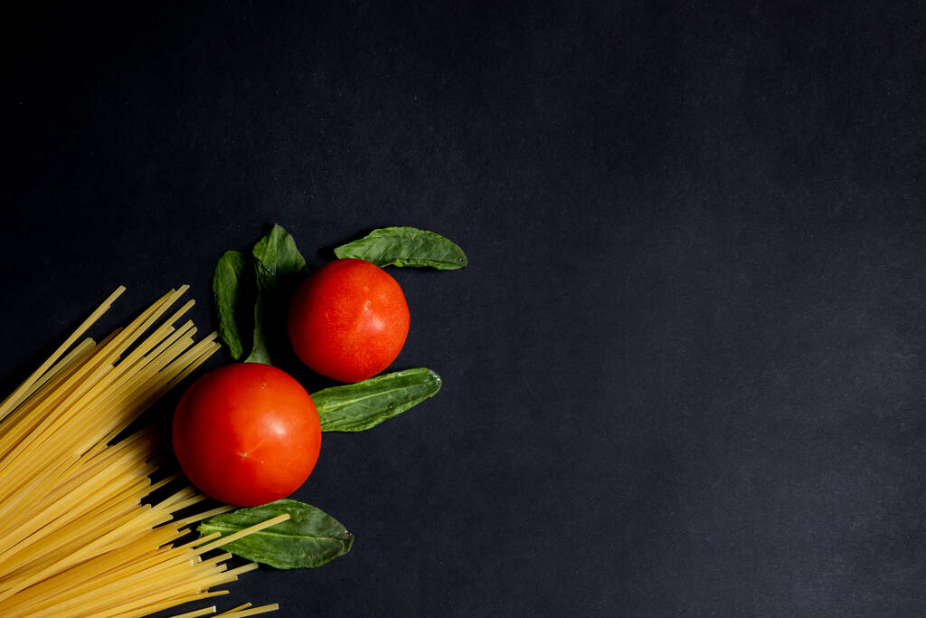 Pasta de espaguetis, tomate y otros productos para cocinar sobre fondo oscuro vista superior. Espacio para texto, vista superior. - Foto, Imagen