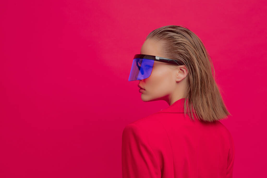 Chladná stylová dívka s módním účesem a stylovými brýlemi s velkým sklem pózuje na jasně červeném pozadí - Fotografie, Obrázek