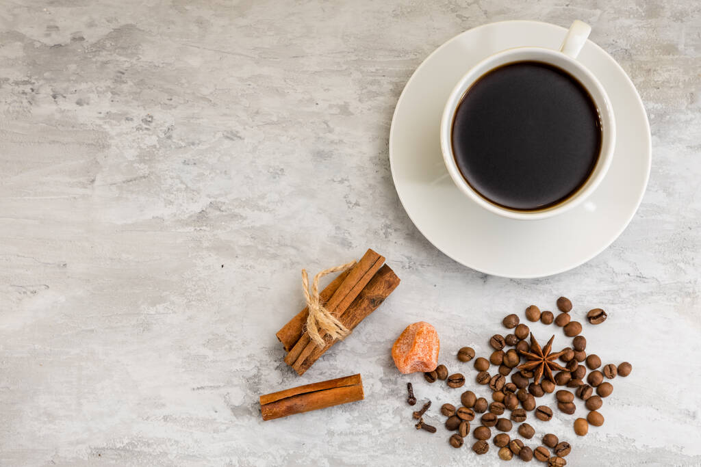 una taza de café negro junto a granos de café, canela y un terrón de azúcar sobre un fondo claro
.  - Foto, Imagen