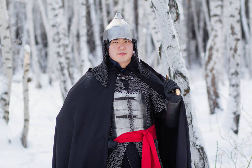   チェーンメールで中世の戦士,ヘルメット,冬の白樺の森の背景に彼の手にサーベルと黒のマント. - 写真・画像