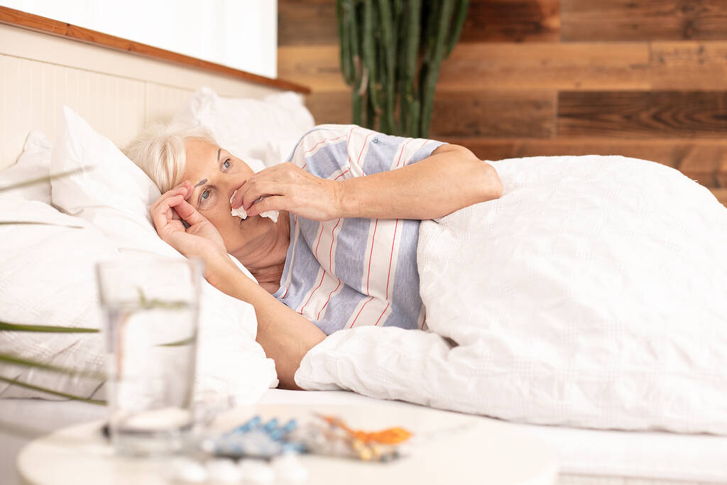 Εποχιακή γρίπη. Άρρωστη ηλικιωμένη γυναίκα με πυρετό και μύτη που τρέχει στο κρεβάτι, στο σπίτι. - Φωτογραφία, εικόνα