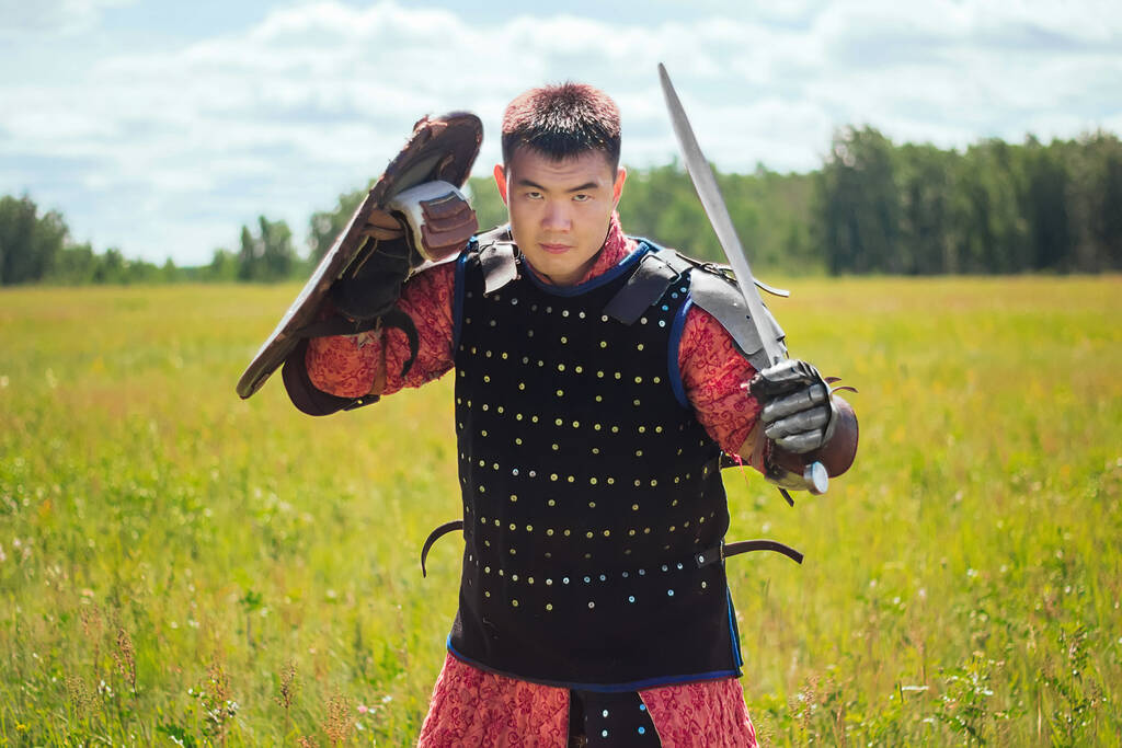 Середньовічний азійський воїн-кочівник у обладунках стоїть у оборонній позиції з щитом і мечем у руках у степу на тлі лісу. Концепція арт-битви в полі. - Фото, зображення