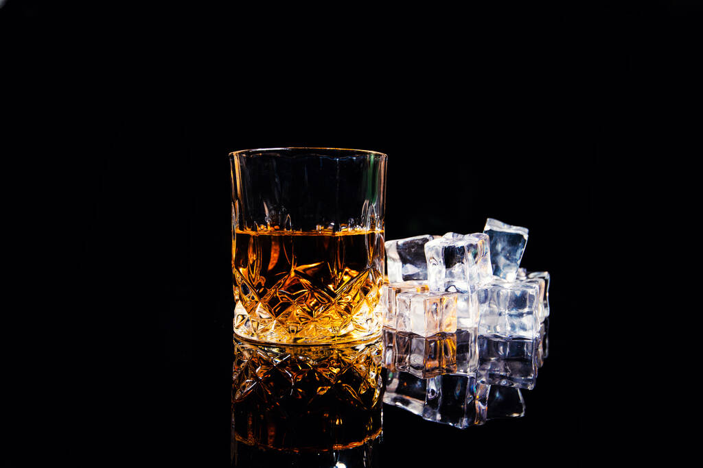 whiskey met ijsblokjes op zwarte achtergrond - Foto, afbeelding
