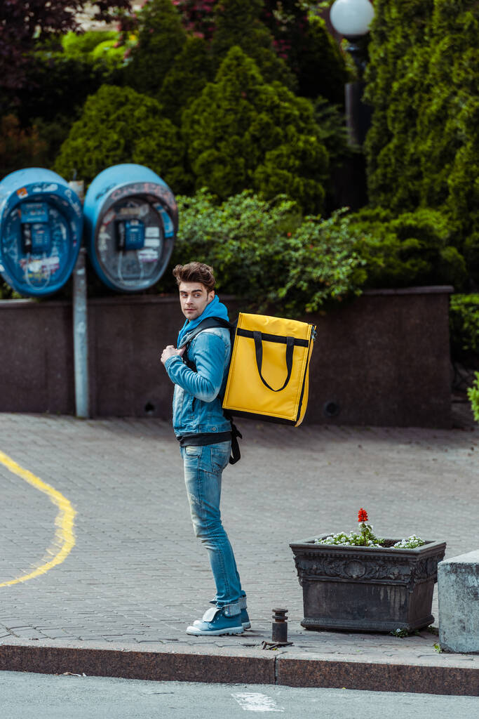 Vista lateral do homem de entrega com mochila térmica em pé na rua urbana
  - Foto, Imagem