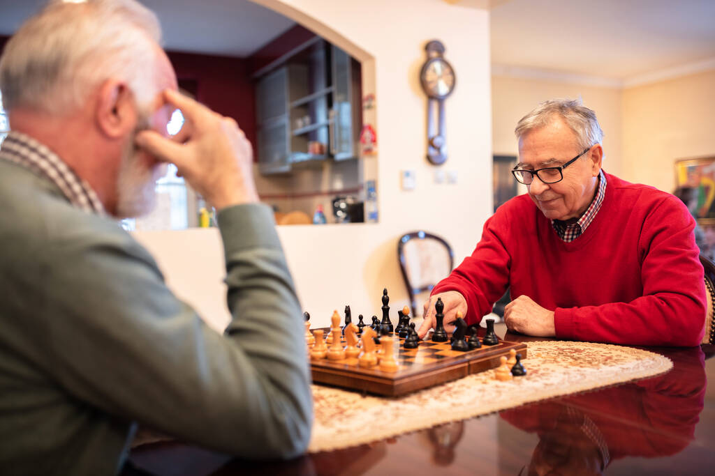 Δύο ανώτεροι άνδρες κάνουν ελιγμούς ενώ παίζουν σκάκι, οι ανώτεροι μένουν σπίτι. - Φωτογραφία, εικόνα