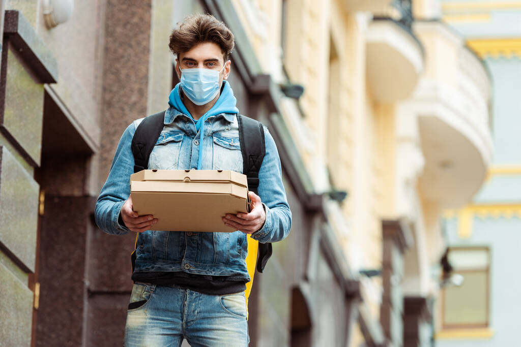 Entrega homem em máscara médica segurando caixas de pizza na rua urbana
  - Foto, Imagem