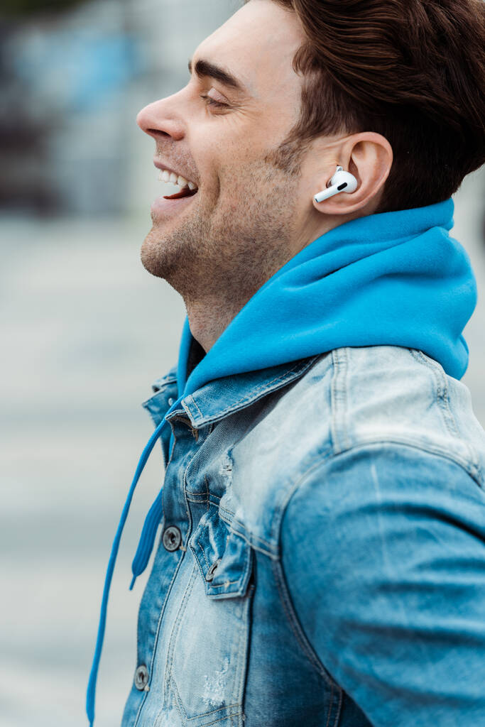 Πλευρική άποψη του ευτυχισμένος άνθρωπος στα ακουστικά γέλιο σε εξωτερικούς χώρους  - Φωτογραφία, εικόνα