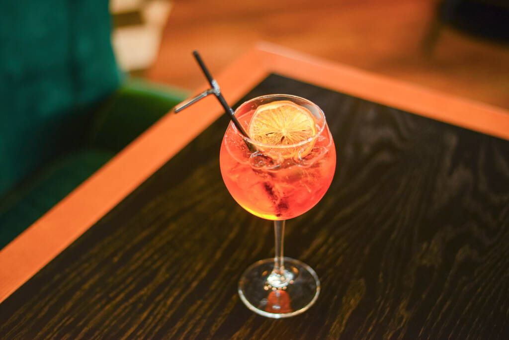 Koude zomer alcohol cocktail met ijs en sinaasappel in een hoog glas op houten tafel op wazig restaurant achtergrond. - Foto, afbeelding