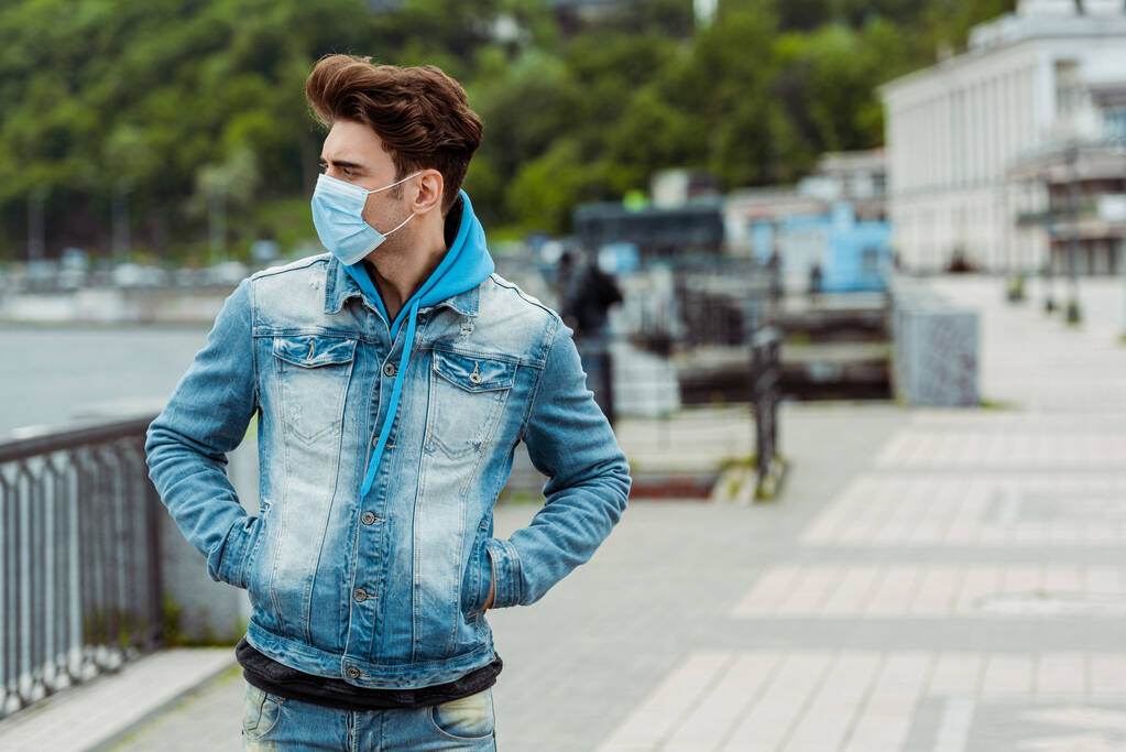 Orvosi maszkos fiatalember, félrenéz a városi utcában.  - Fotó, kép