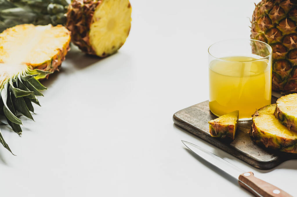 Bardakta taze ananas suyu, beyaz arka planda bıçakla ahşap kesme tahtasındaki lezzetli meyvelerin yanında. - Fotoğraf, Görsel