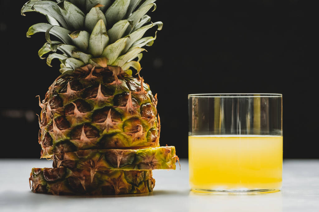 свежий ананасовый сок и срезать вкусные фрукты на белой поверхности на черном фоне
 - Фото, изображение