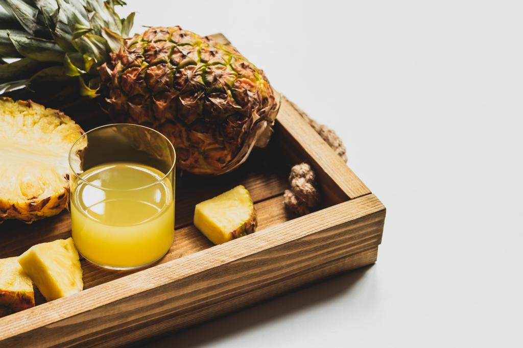 čerstvý ananasový džus a řezané lahodné ovoce na dřevěném podnosu na bílém pozadí - Fotografie, Obrázek