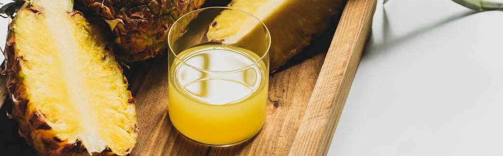 свежий ананасовый сок и срезать вкусные фрукты на деревянном подносе на белом фоне, панорамная ориентация
 - Фото, изображение