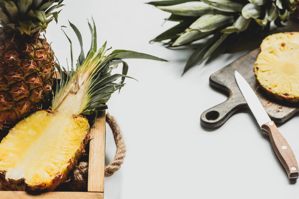 szelektív fókusz friss vágott ananász fa tálca és vágódeszka kés fehér háttér - Fotó, kép