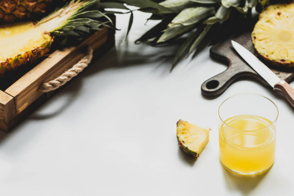 新鮮なパイナップルジュースの選択的な焦点と木のトレイにおいしい果物をカットし、白い背景にナイフでまな板 - 写真・画像