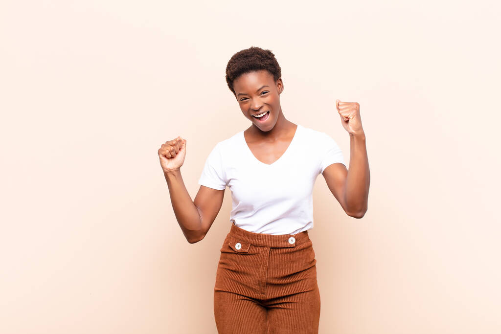 junge hübsche schwarze Frau fühlt sich glücklich, positiv und erfolgreich, feiert Sieg, Erfolge oder viel Glück - Foto, Bild