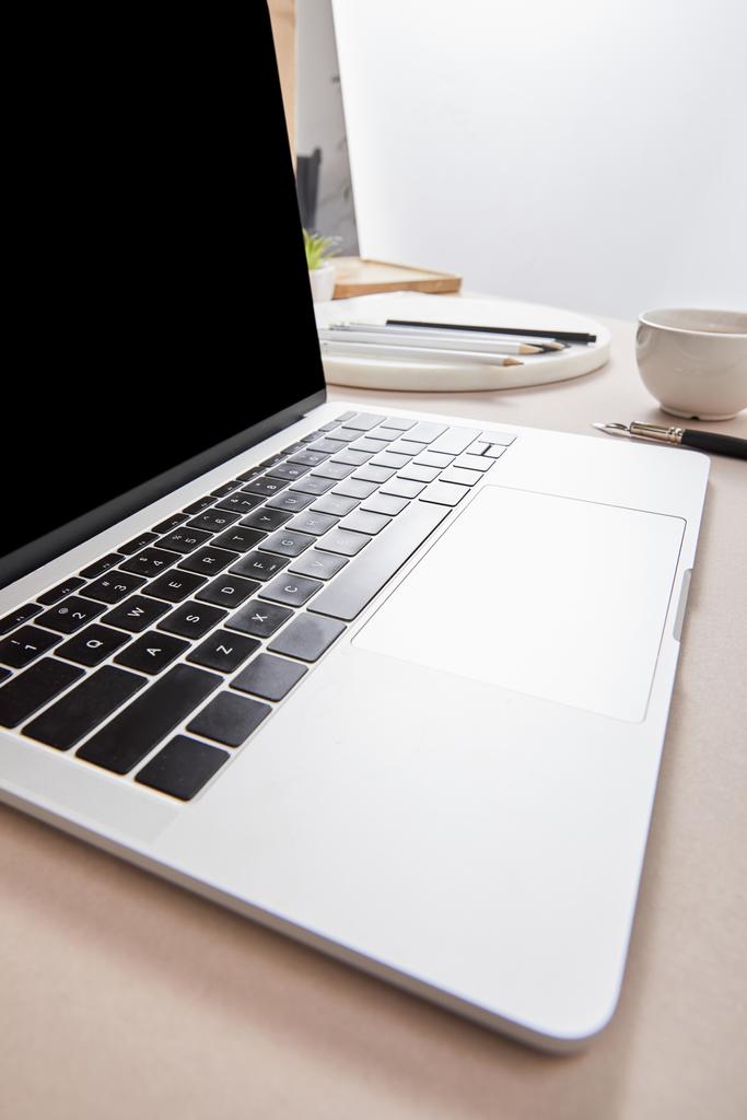 Laptop mit leerem Bildschirm bei Tasse Tee und Schreibwaren auf beiger Oberfläche - Foto, Bild