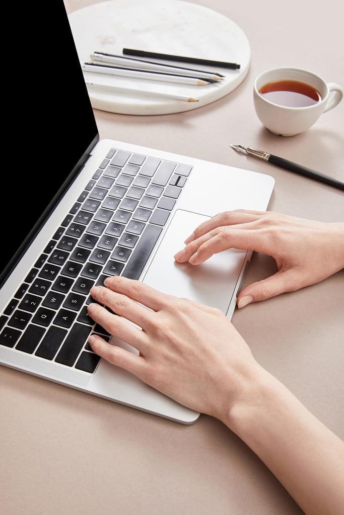 cropped view of woman using laptop near cup of tea on beige surface - Photo, Image