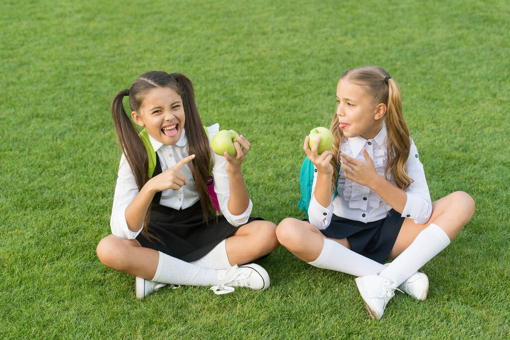 Ízlelgetem a citromot. Egy kislány rámutatott a savanyú almára. Gyümölcssav. A kisgyerekek zöld füvön esznek gyümölcsöt. Iskolai nasi. Organikus vitaminok. Egészséges étel. Iskola egészsége és táplálkozása - Fotó, kép