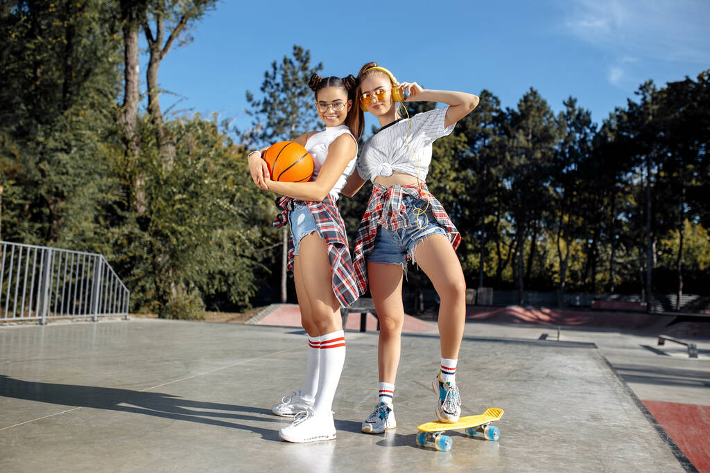 Zwei aufgeweckte junge Mädchen im Teenageralter posieren mit glücklichen Gesichtern im Skatepark. Konzept Freiheit und beste Freunde. - Foto, Bild