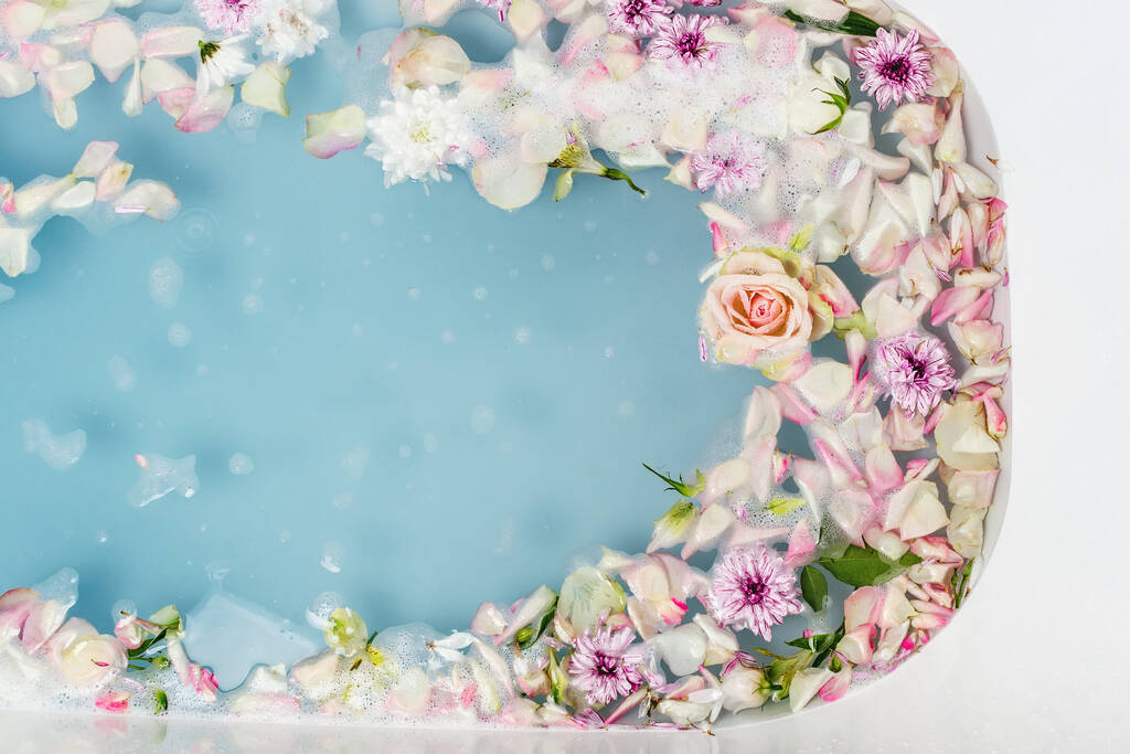 Top view of bath filled with blue bubble water, flowers and petals, spa or selfcare concept - Photo, Image