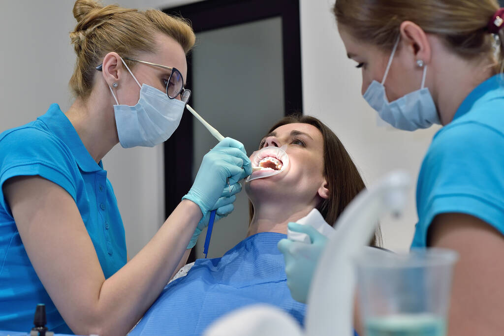 Nainen Hammaslääkäri ja avustava tutkia potilaan kanssa hammasraudat hammashoitolassa. Hammashoidon käsite - Valokuva, kuva