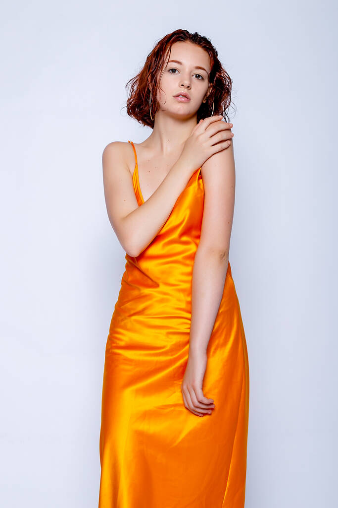 Portret atrakcyjnej dziewczyny w pomarańczowej sukience w studio. Fascynująca rudowłosa pani. - Zdjęcie, obraz