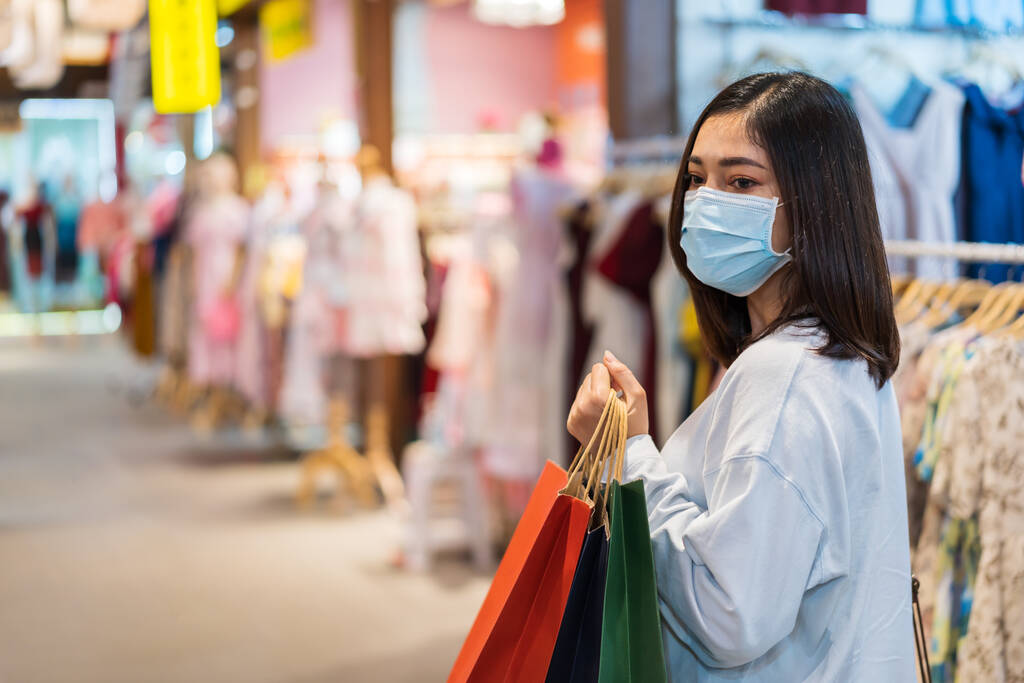 jeune femme tenant un sac à provisions et regardant des vêtements au centre commercial et son masque médical pour la prévention de la pandémie de coronavirus (Covid-19). nouveaux concepts normaux
 - Photo, image