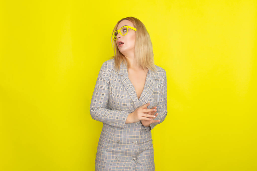 Atractiva mujer rubia en vestido de chaqueta a cuadros sobre fondo amarillo con gafas amarillas
 - Foto, Imagen