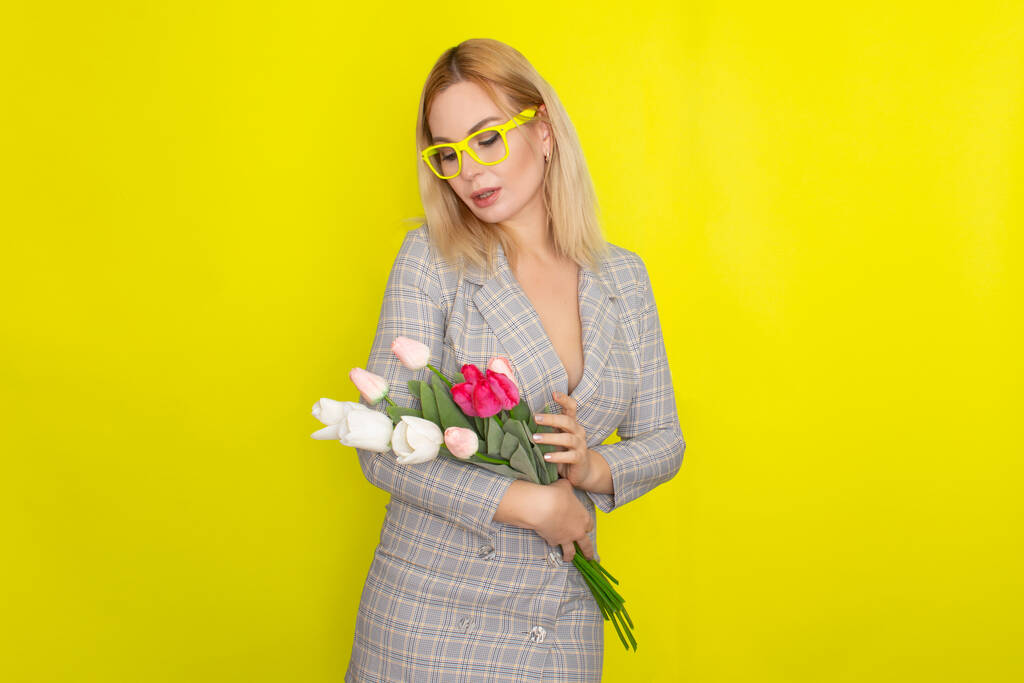 Блондинка в клетчатом платье держит букет тюльпанов на желтом фоне
 - Фото, изображение