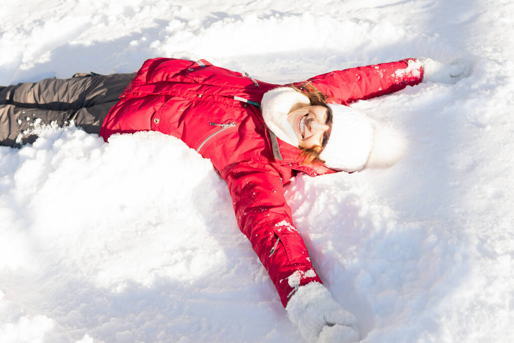 Una chica con una chaqueta roja yace en la nieve. Ella esquía. Una mujer atractiva está caminando en el bosque
 . - Foto, Imagen