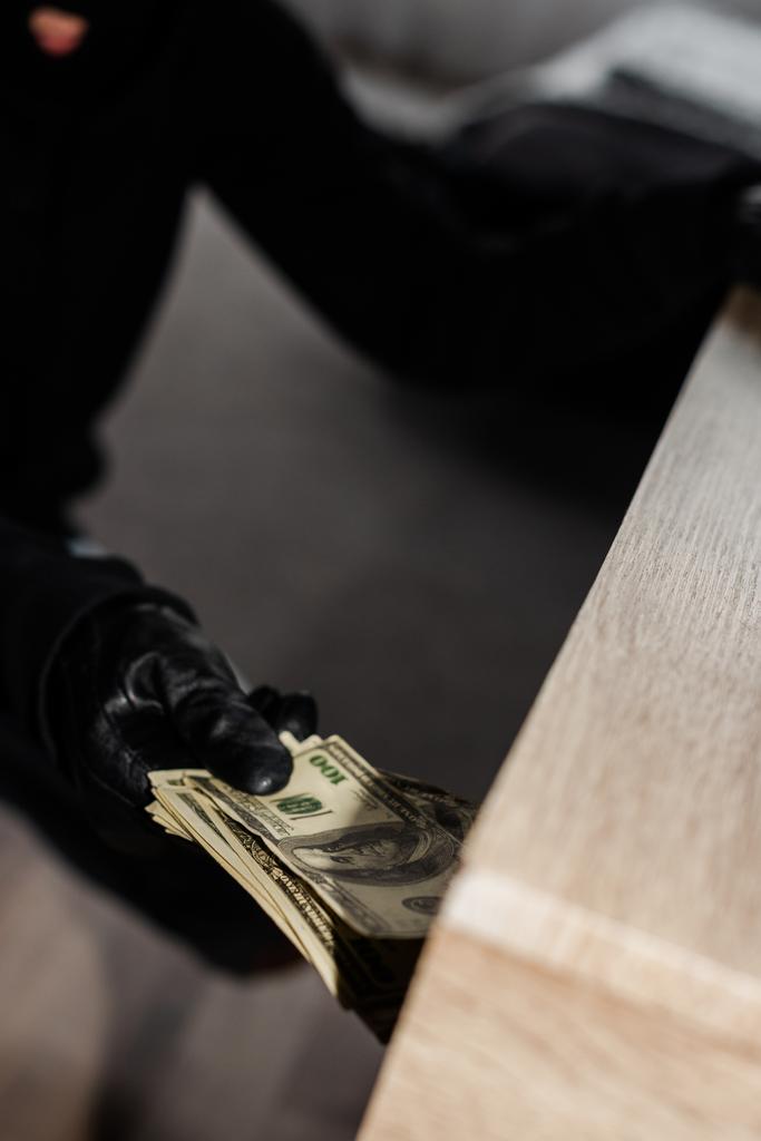 Selective focus of robber in leather glove taking dollars from table   - Photo, Image