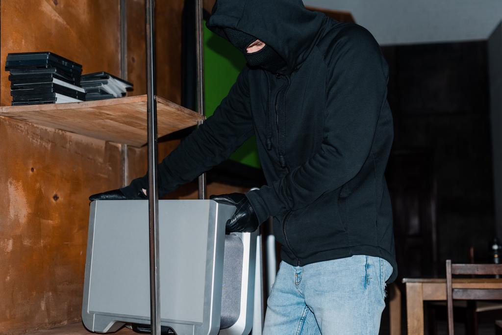 Rapinatore in passamontagna che prende altoparlante wireless da armadio durante il furto
  - Foto, immagini