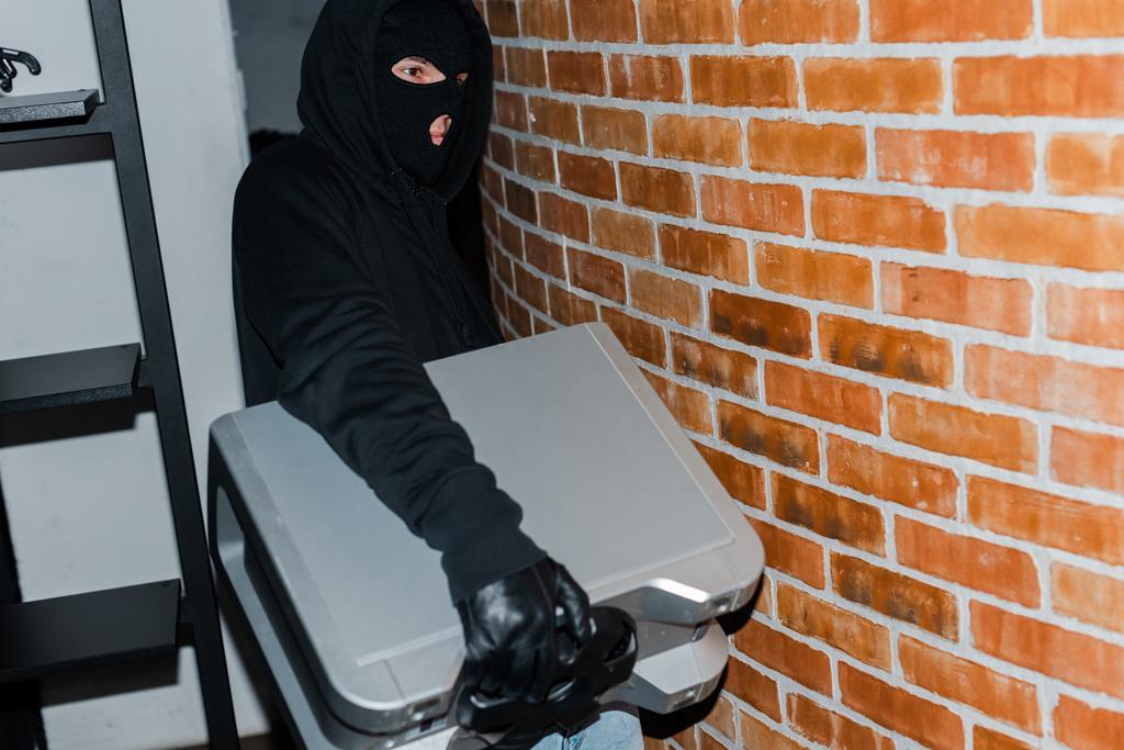 Ladro in pelle guanto e passamontagna tenendo altoparlante wireless durante il furto
  - Foto, immagini