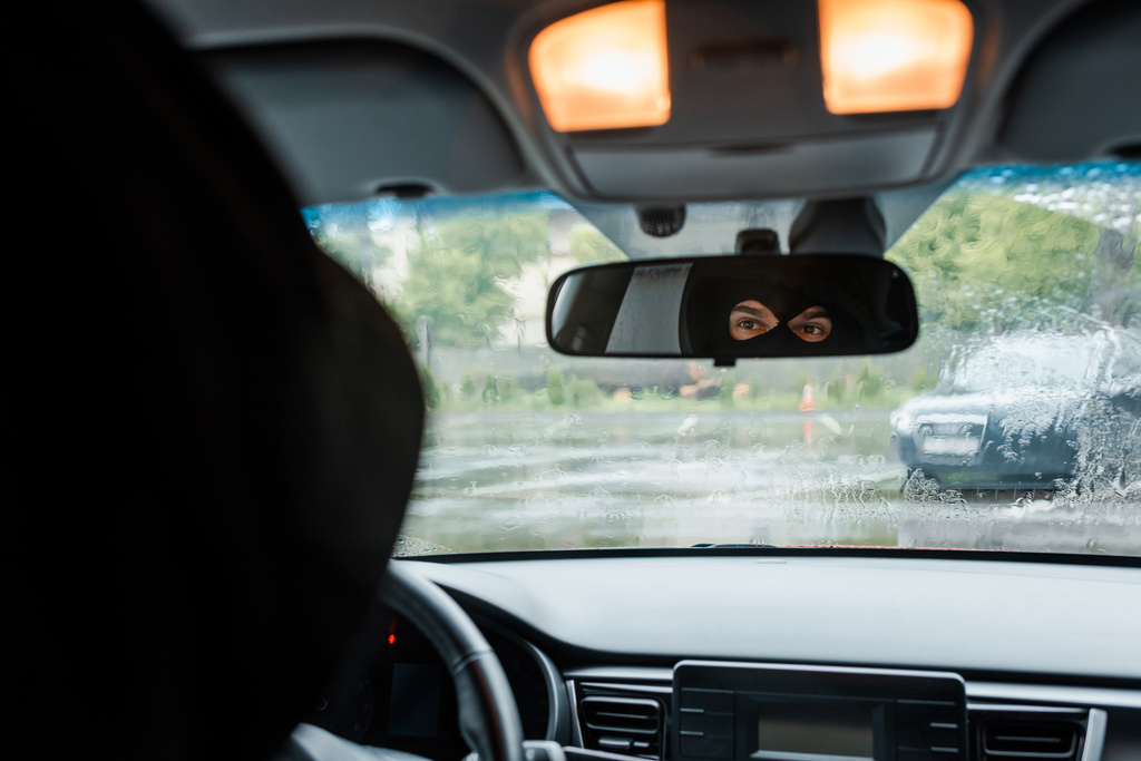 Селективный фокус человека в балаклаве, смотрящего на зеркало в машине
  - Фото, изображение