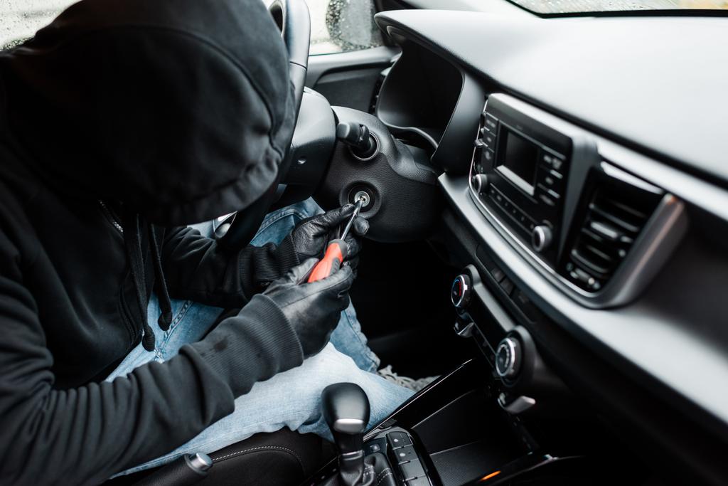 Foco seletivo do ladrão segurando chave de fenda perto de bloqueio de ignição no carro
 - Foto, Imagem