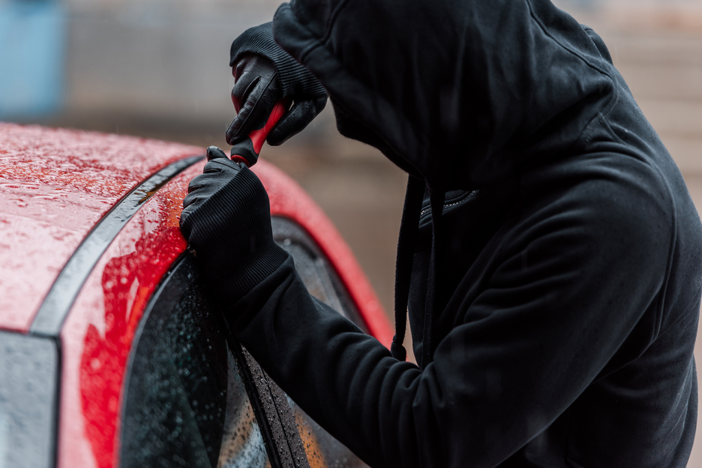 Επιλεκτική εστίαση του ληστή στη μάσκα κρατώντας κατσαβίδι κατά το άνοιγμα γυαλί της πόρτας του αυτοκινήτου  - Φωτογραφία, εικόνα