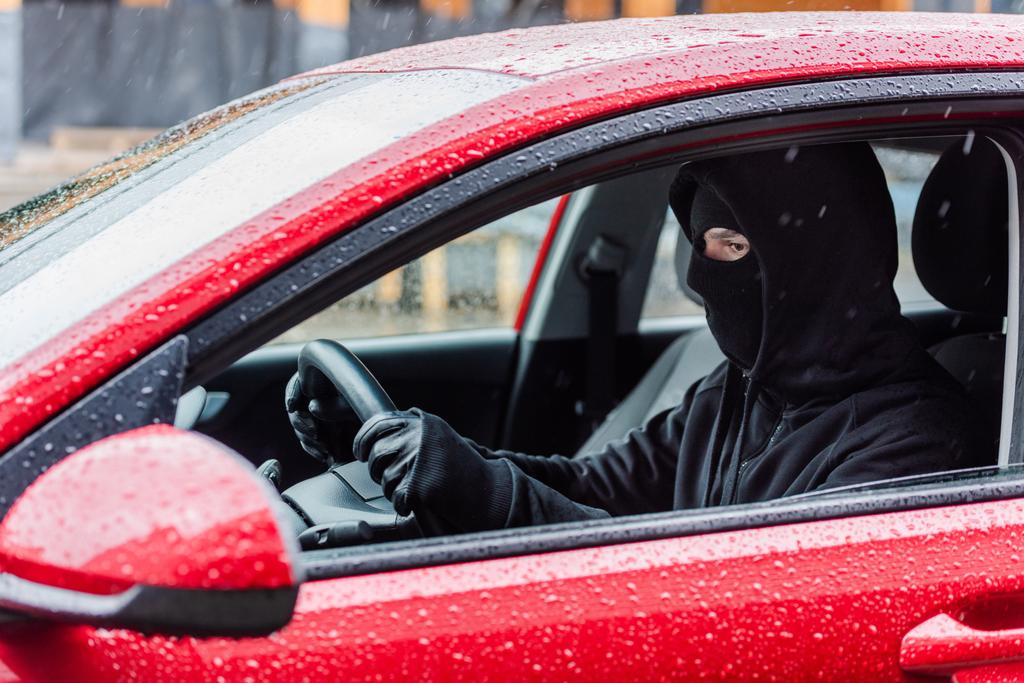 Oldalnézet rabló bőrkesztyűben és maszk ül az autóban esőben  - Fotó, kép