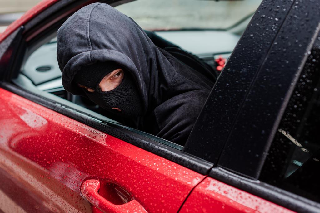 Selective focus of robber in balaclava looking away while sitting in car  - Photo, Image