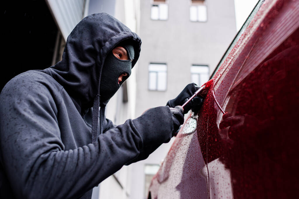 Выборочный фокус грабителя с помощью отвертки при открытии двери автомобиля на городской улице
  - Фото, изображение