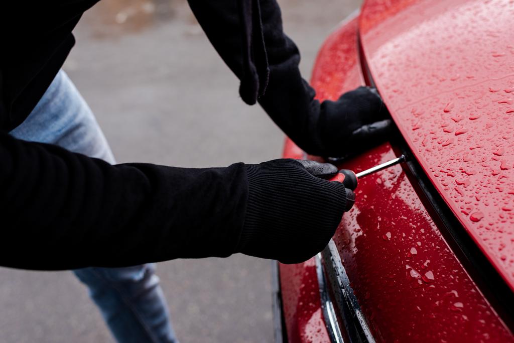 Обрізаний вид грабіжника в шкіряних рукавичках з використанням викрутки під час відкриття автомобільної витяжки на міській вулиці
  - Фото, зображення