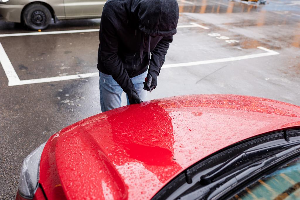 Грабитель в кожаных перчатках держит отвертку и открывает капот на городской улице
  - Фото, изображение