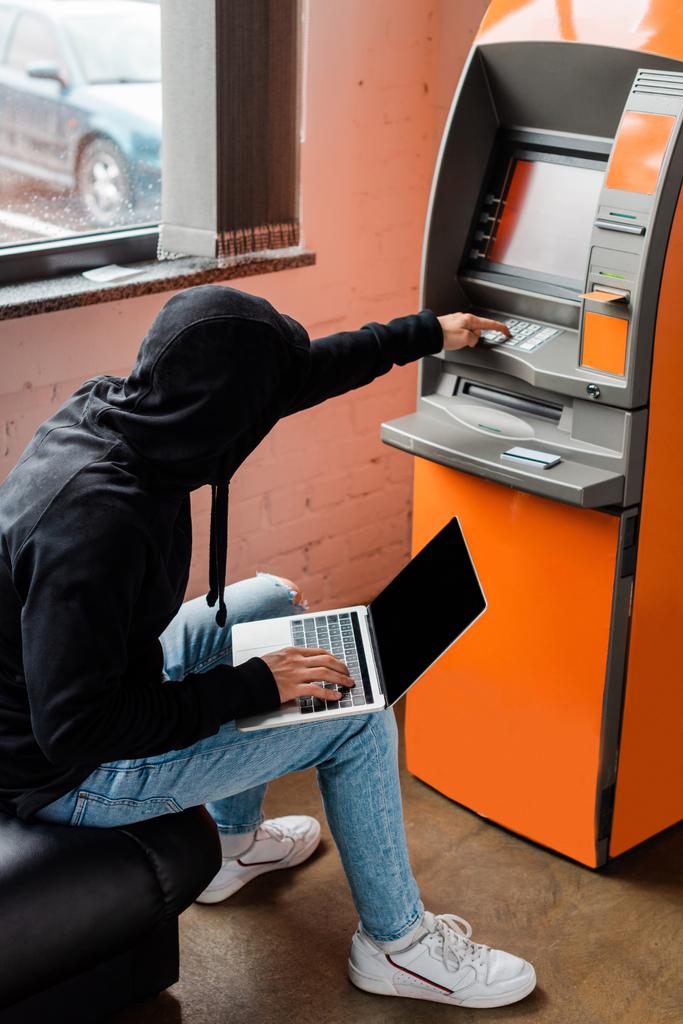 A betörő oldalnézete laptoppal és ATM-mel a rablás során  - Fotó, kép