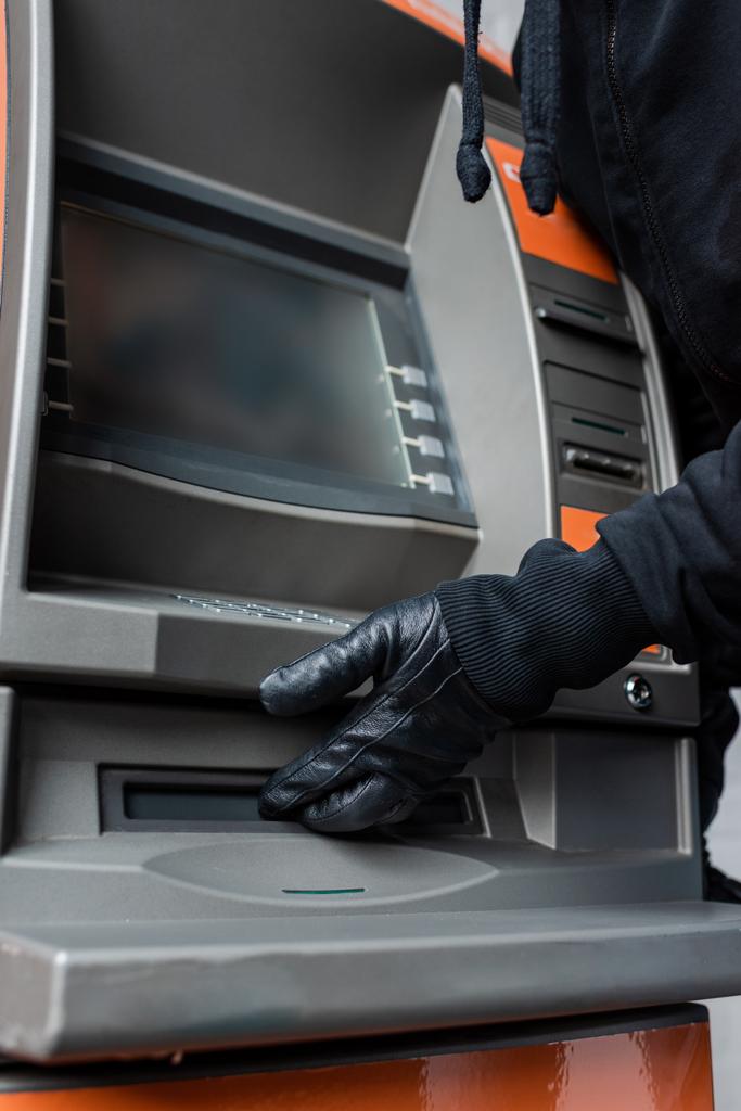 Vágott kilátás tolvaj bőrkesztyűben fogja a kezét pénzkiadó automata közelében  - Fotó, kép