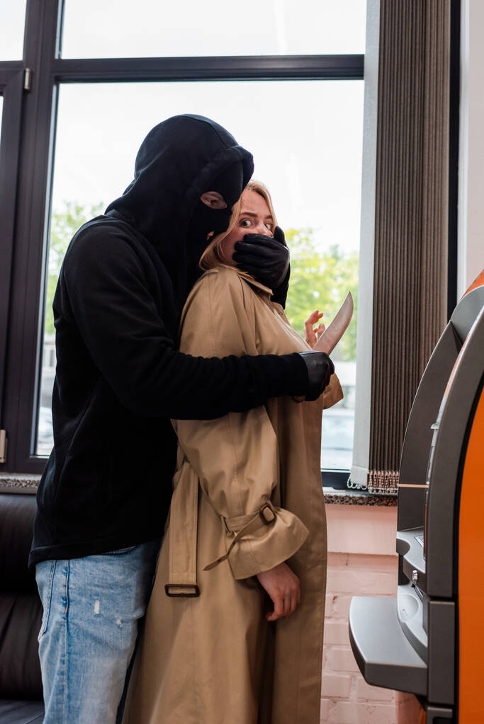 Oldalnézet a rabló kezében kés közelében ijedt nő mellett ATM  - Fotó, kép
