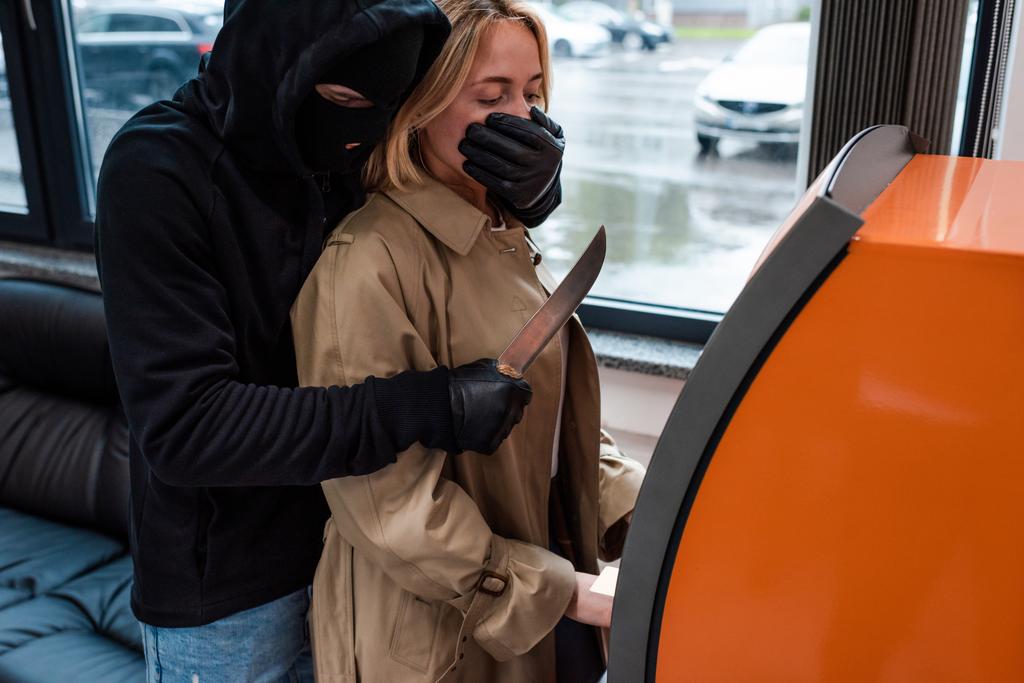 Räuber mit Maske hält Messer in der Nähe von Frau mit Geldautomat  - Foto, Bild